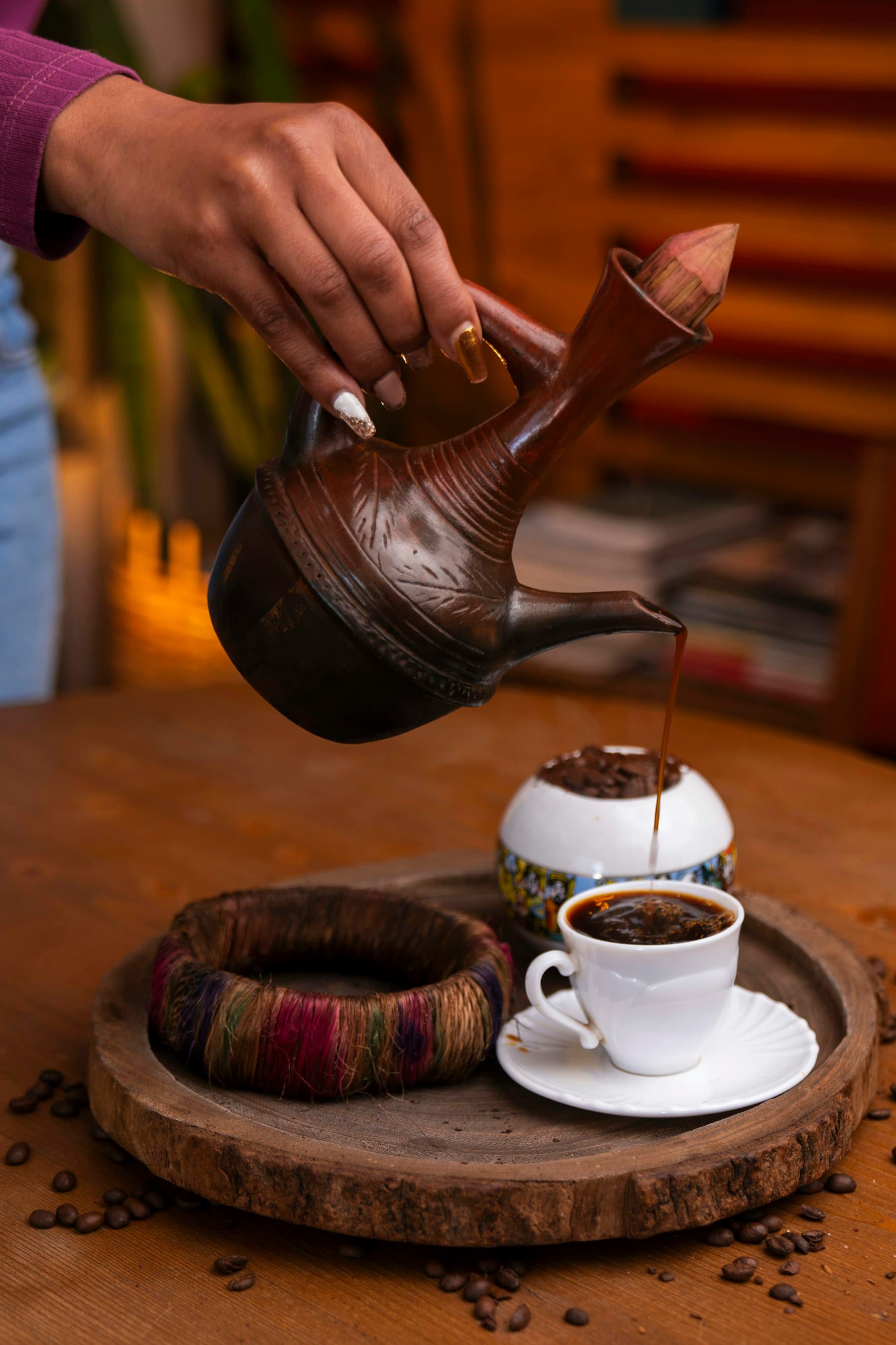 Coffee being poured from a decorated clay pot into a small cup
