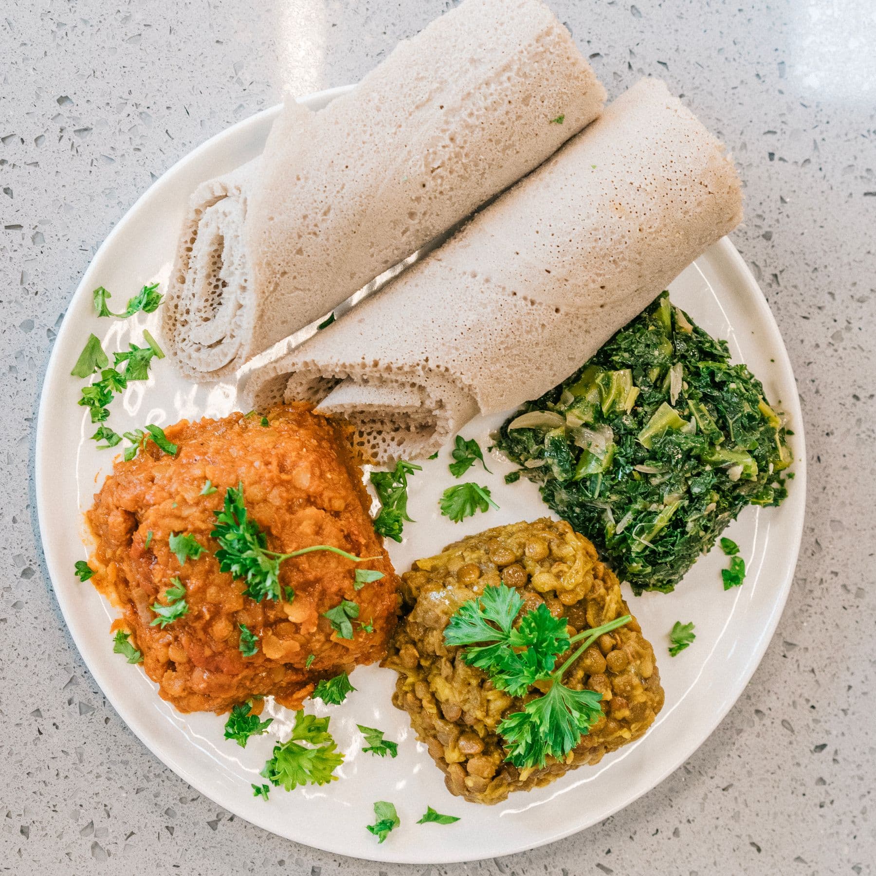 Injera served with red lentils, green lentils, and cooked greens